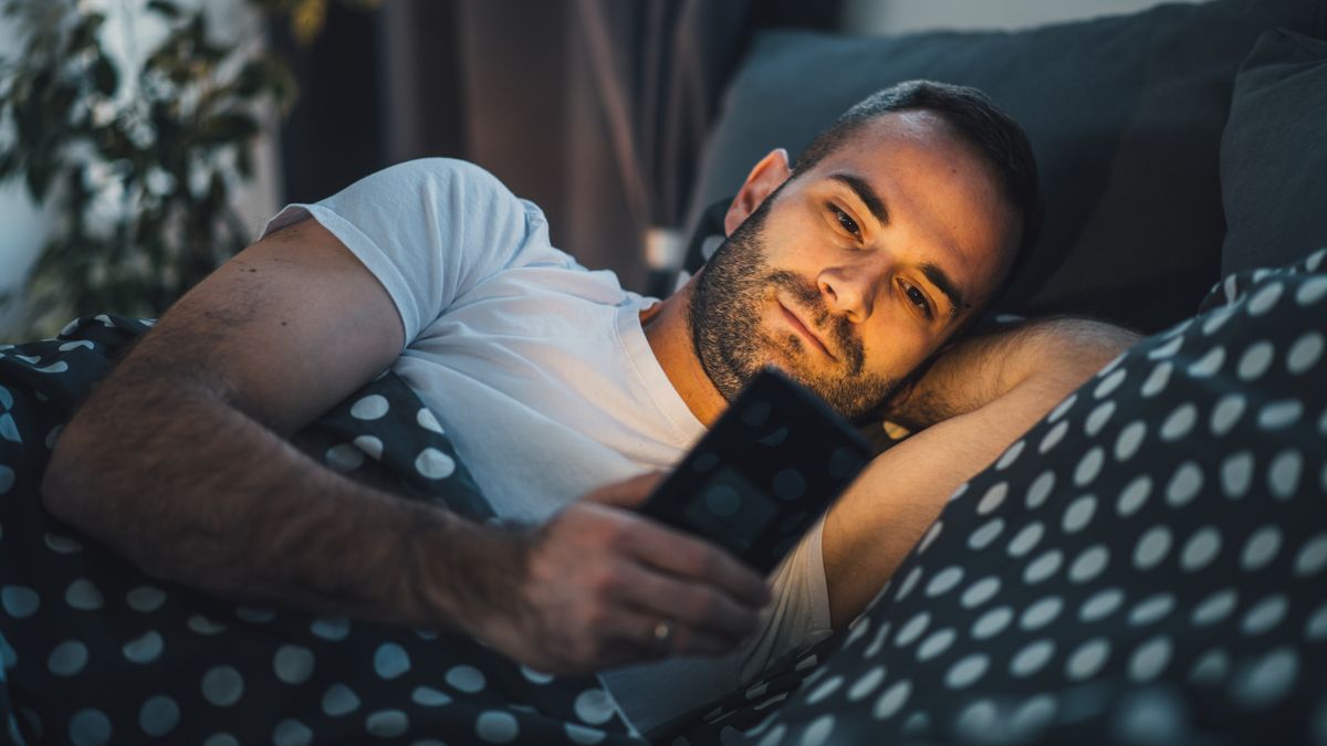 Man using a smartphone while lying in bed.