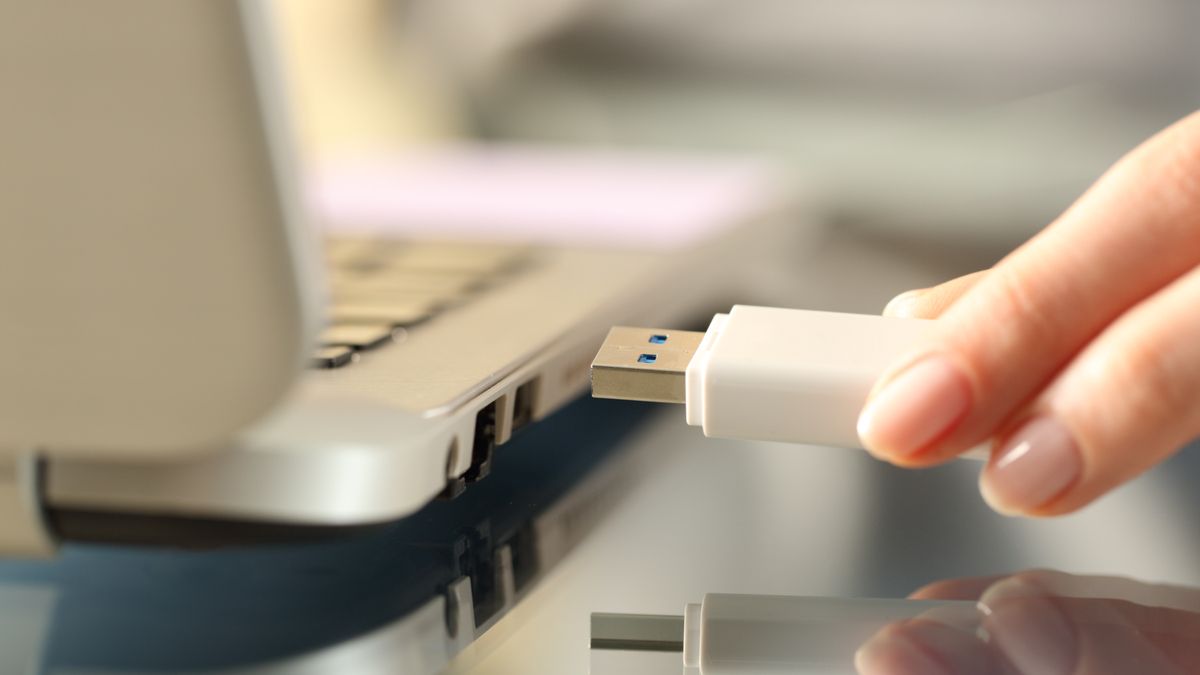 Closeup of a woman's hand plugging a USB drive into a laptop.