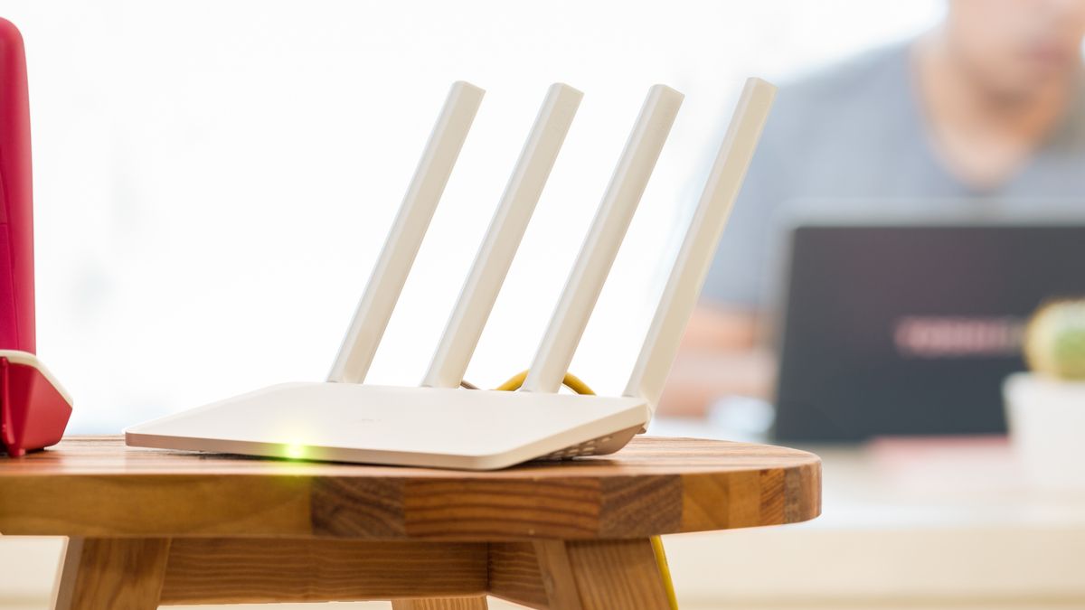 White Wi-Fi router on a tabletop with a man using a laptop in the background.