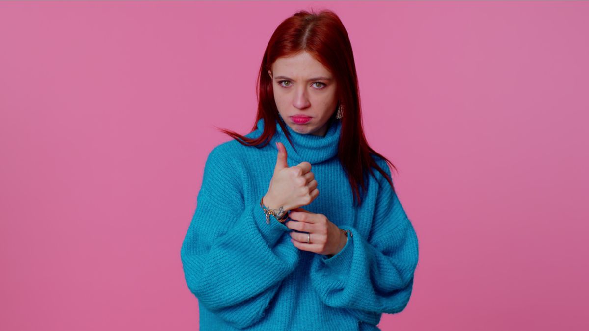 A young woman in a blue sweater giving a thumbs-up gesture.