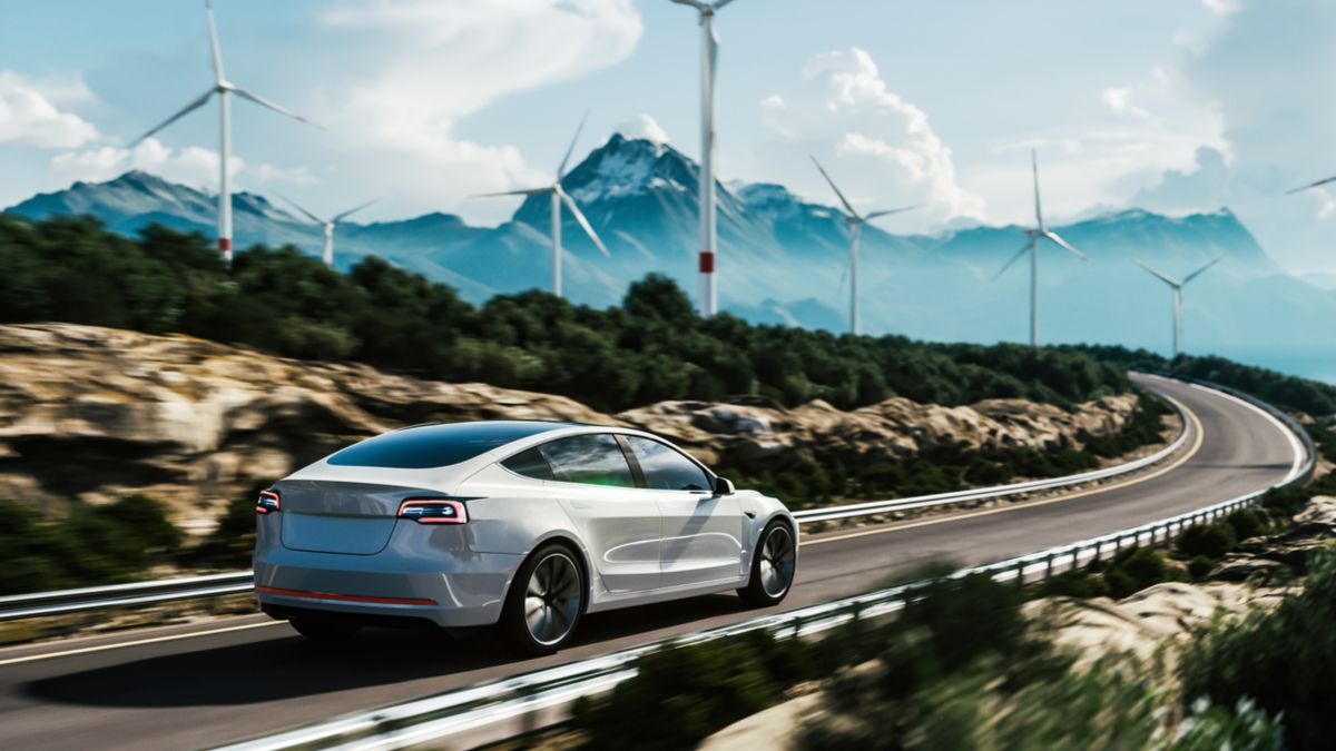 An electric car driving down a road with wind turbines in the background.
