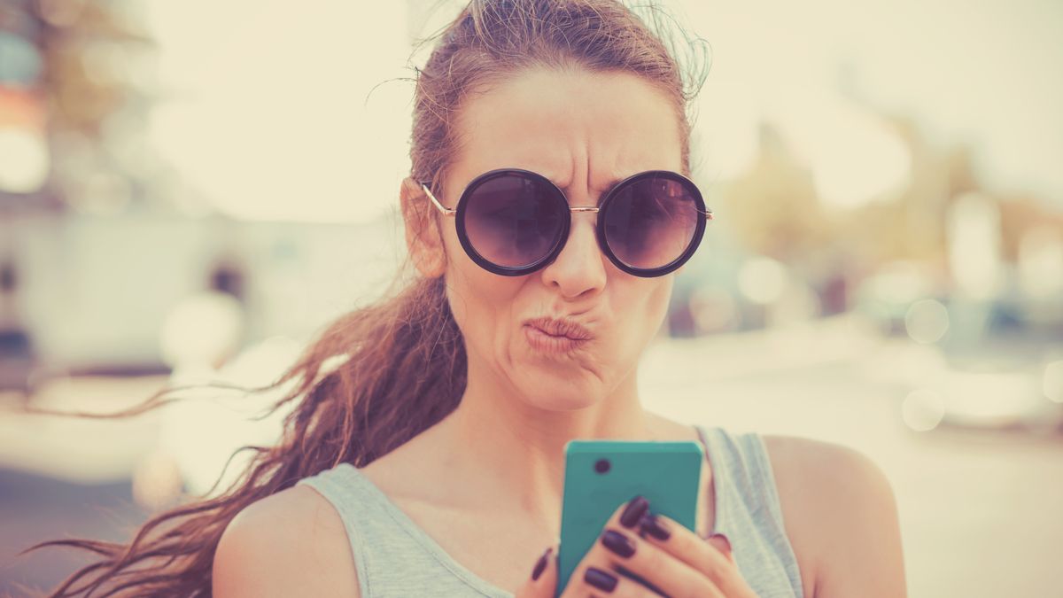 Woman looking at her smartphone with a displeased or skeptical expression.