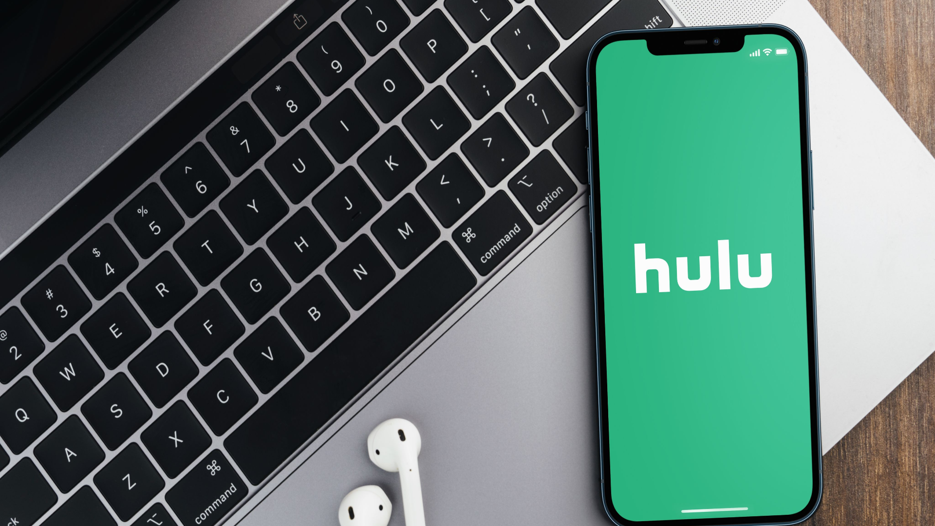 Hulu app on the smartphone screen on wooden background with a computer beside it. Top view.