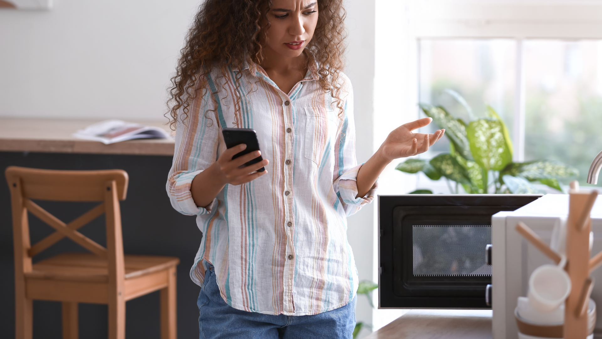 Upset person holding mobile phone near open microwave in modern kitchen