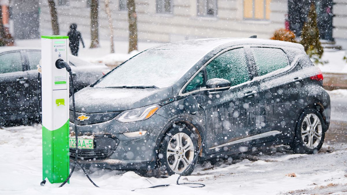 A Chevy Bolt electric car plugged into a charging station as snow falls.