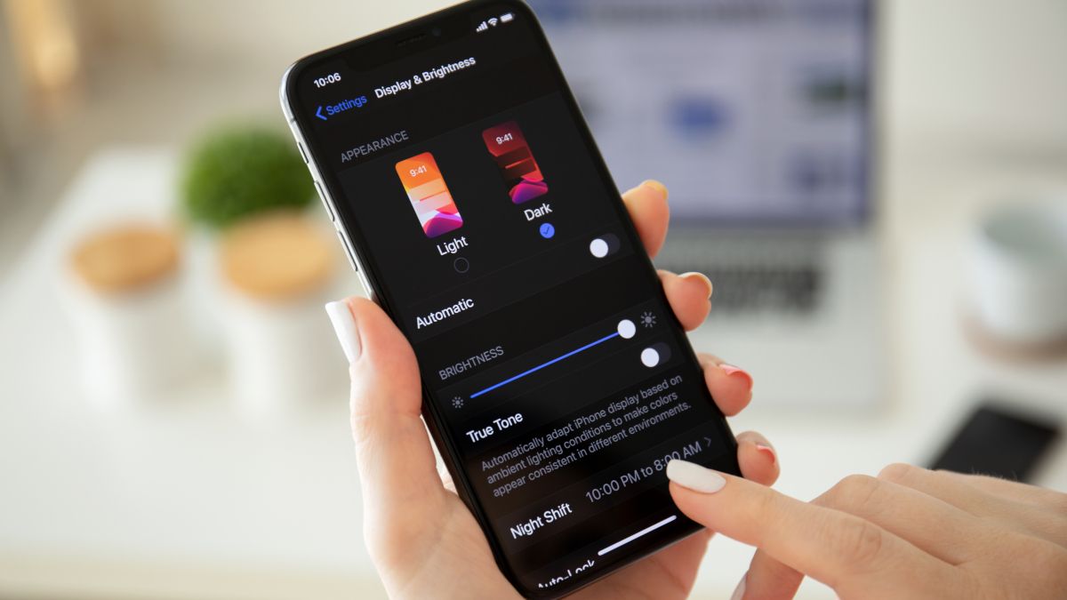 Woman's hands adjusting dark mode settings on an iPhone X.
