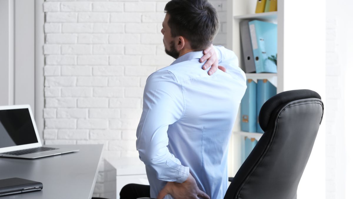 Man sitting in an office chair and clutching his back in pain.