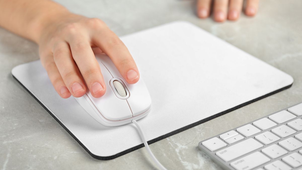 Closeup of a woman's hand using a wired mouse on a white mouse pad.