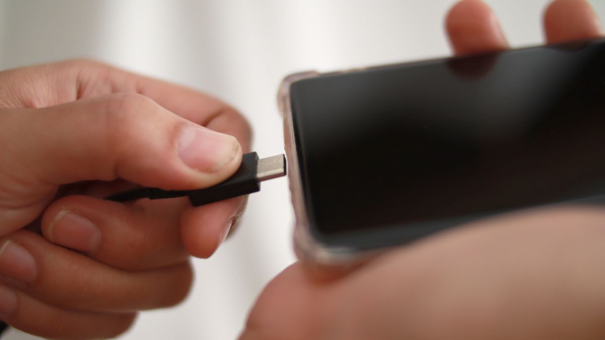 Closeup of a person plugging a USB cord into a smartphone.