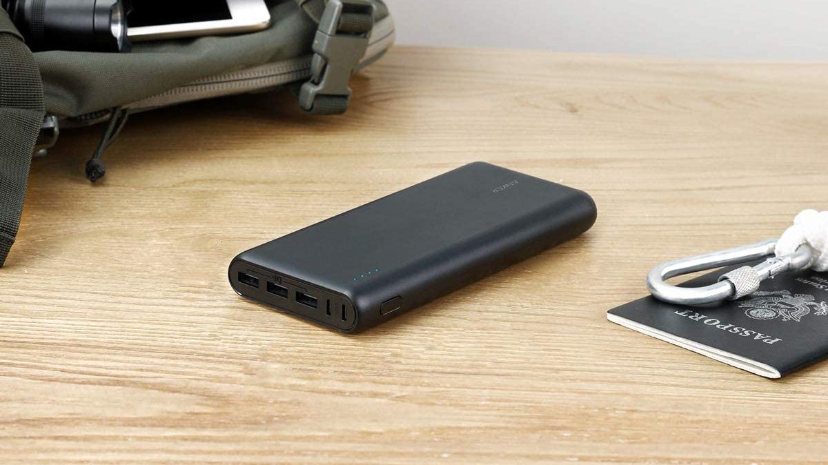 Anker PowerCore 26800 Portable Charger sitting on a wooden desk beside a passport and backpack