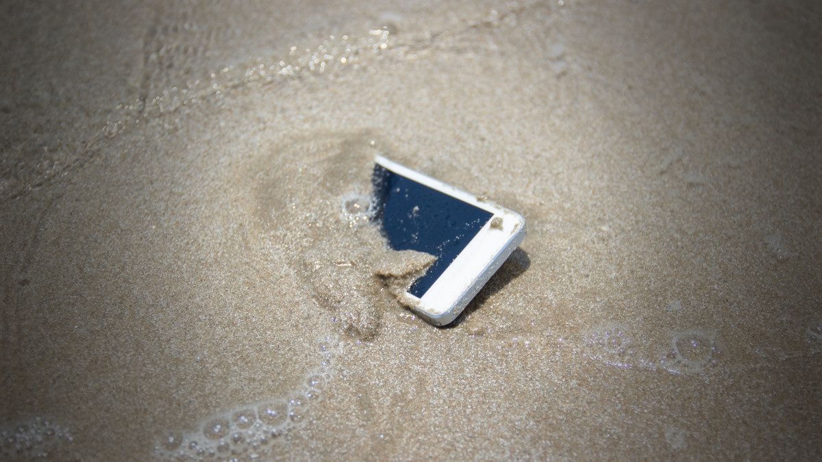 A smartphone in the ocean sand with saltwater.