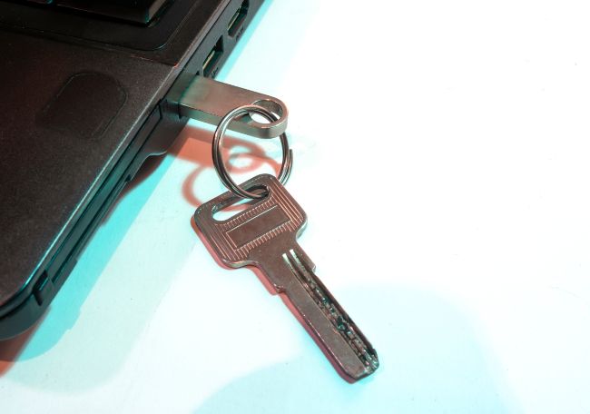 A USB flash drive plugged into a laptop and attached to a key ring with a physical key.