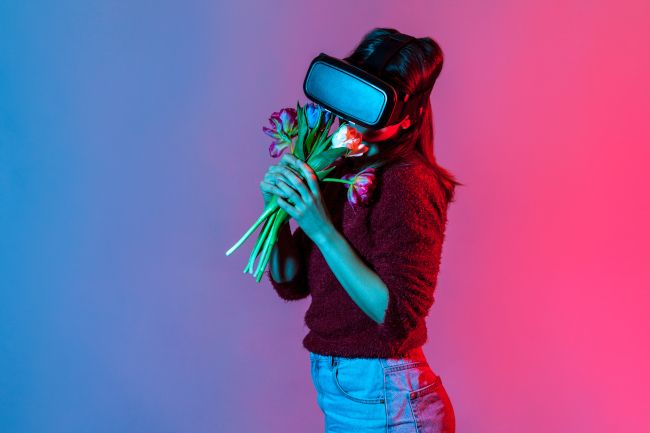 Woman wearing virtual reality headset and enjoying the smell of a bouquet of flowers.