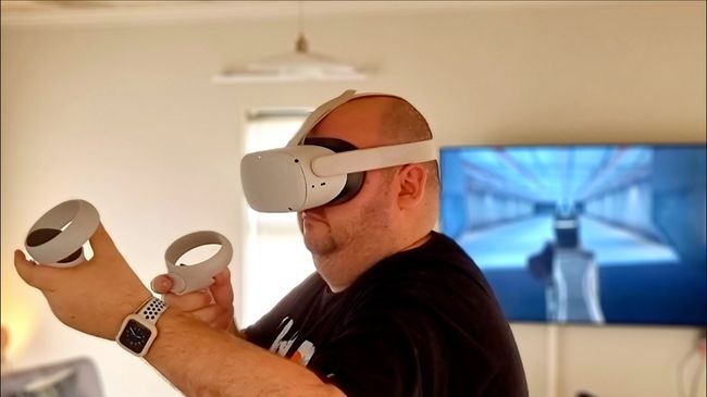 A man using a Quest VR headset with the visuals casting to a TV on the wall.