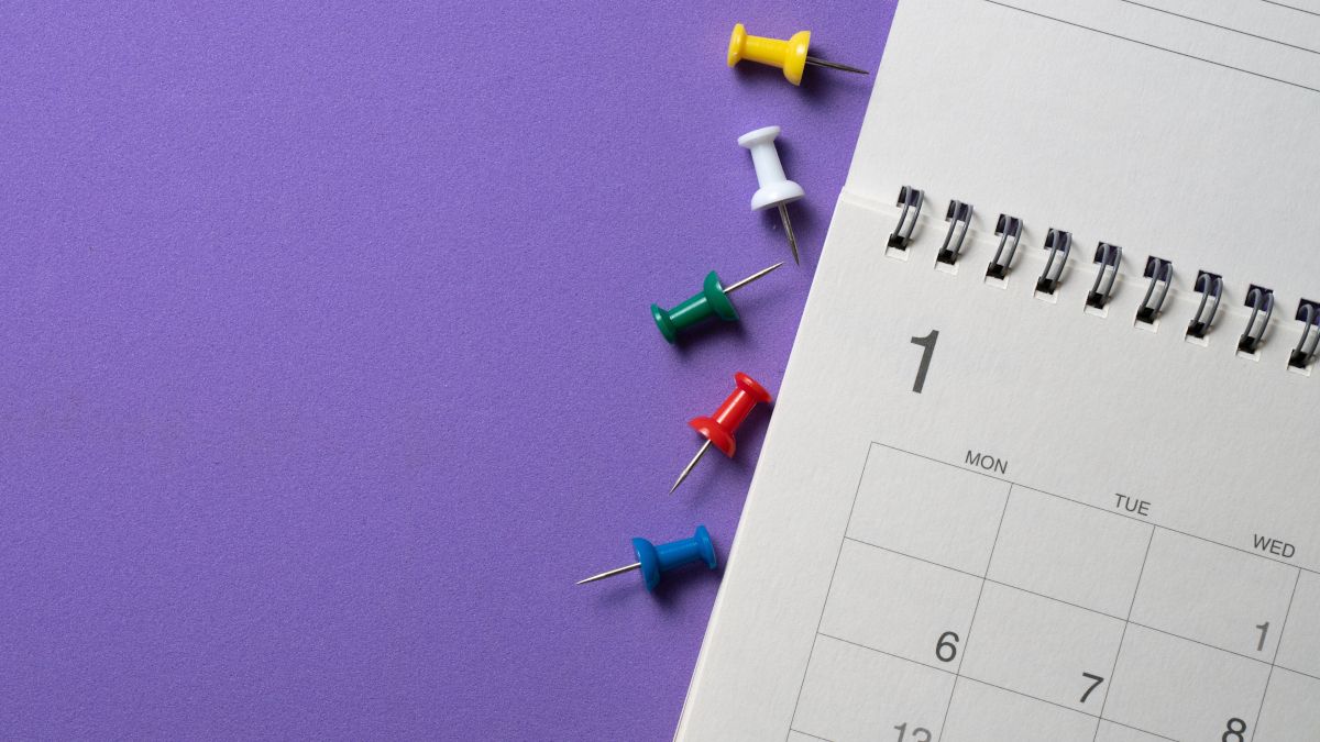 A calendar next to several colorful thumbtacks on a purple surface.