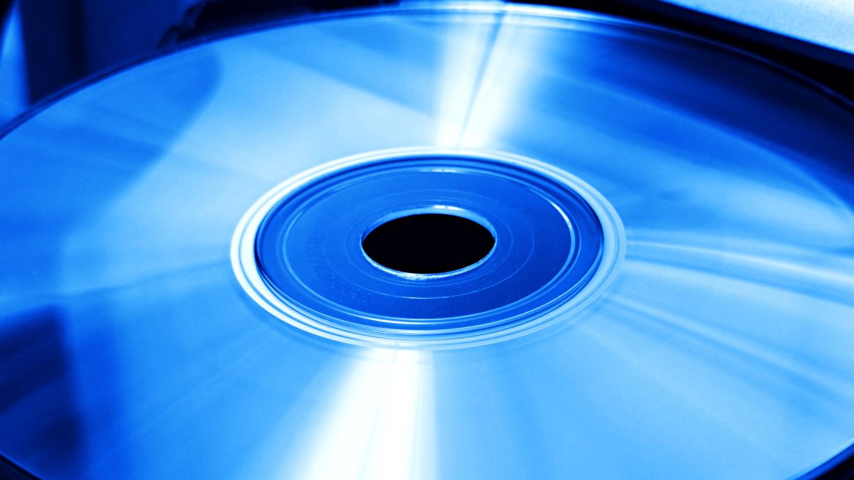 A CD, DVD, or Blu-ray disc in a disc drive under blue light.