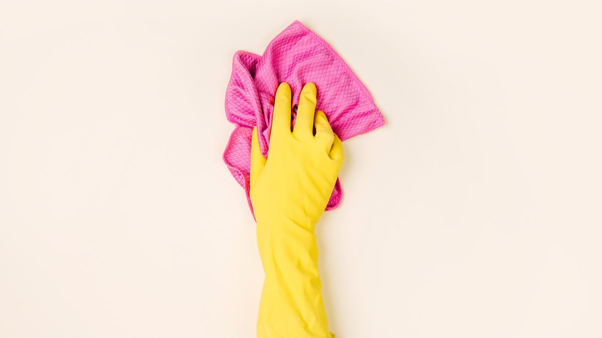 A person's hand wearing a rubber glove and wiping a surface with a pink cloth.