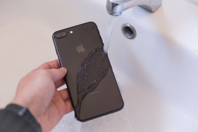 Person holding an iPhone under running water from a tap.