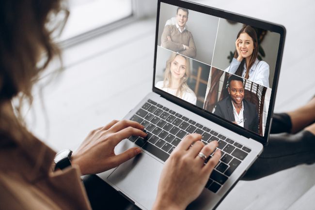 Woman using a laptop with a grid of people in a video conference on-screen.