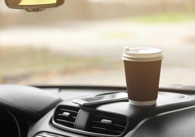 A smartphone and paper coffee cup on top of a car dashboard.