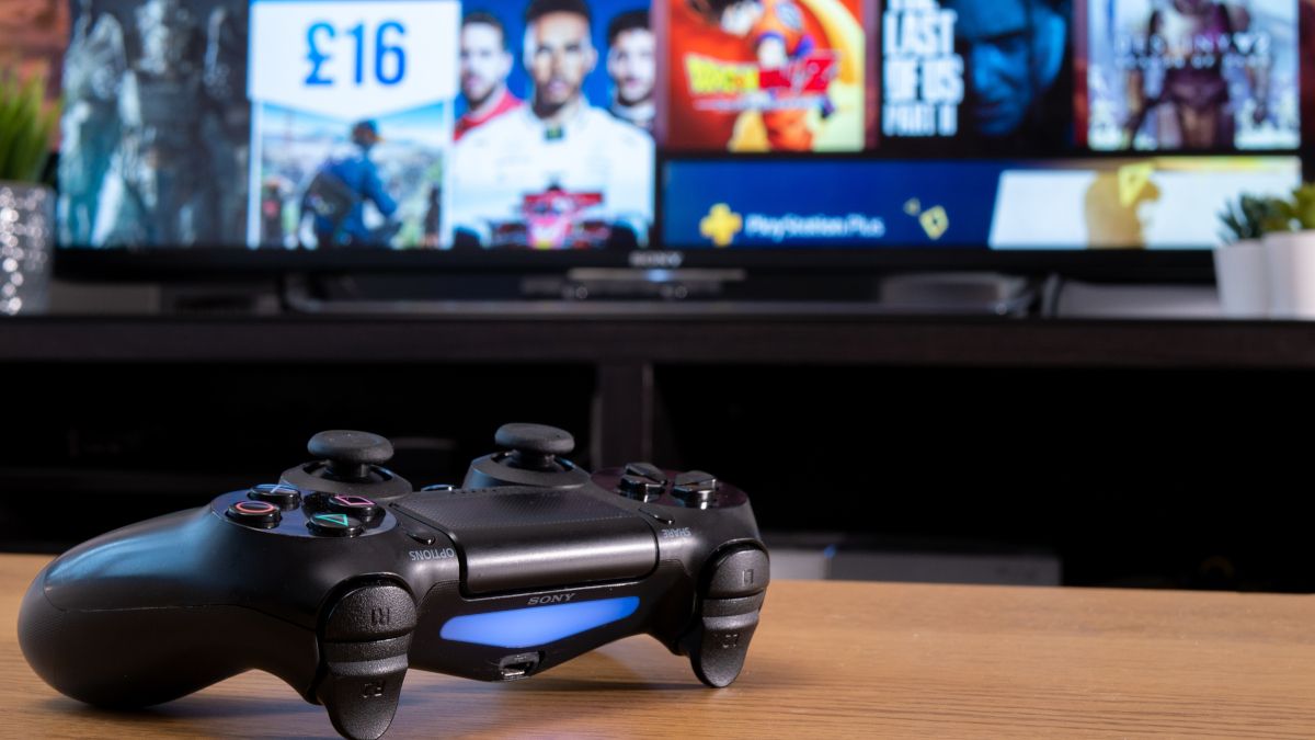 A Sony Dualshock 4 controller in front of a TV showing the PlayStation store.