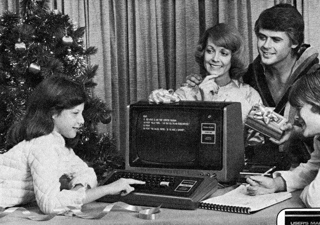 A kid using a TRS-80 computer near a Christmas tree with its parents looking on.