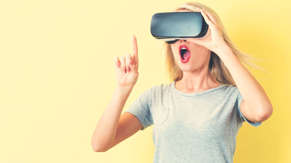 Woman wearing a VR headset and making a surprised expression while reaching out with her index finger.
