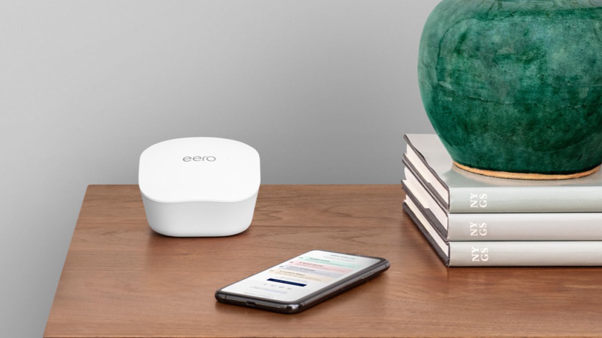 An Amazon Eero mesh extender on a table next to a stack of books and a phone.