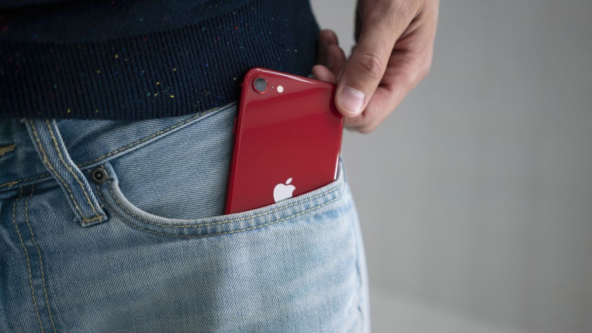 A red iPhone SE (2022 version) being pulled out of a person's jean pocket.