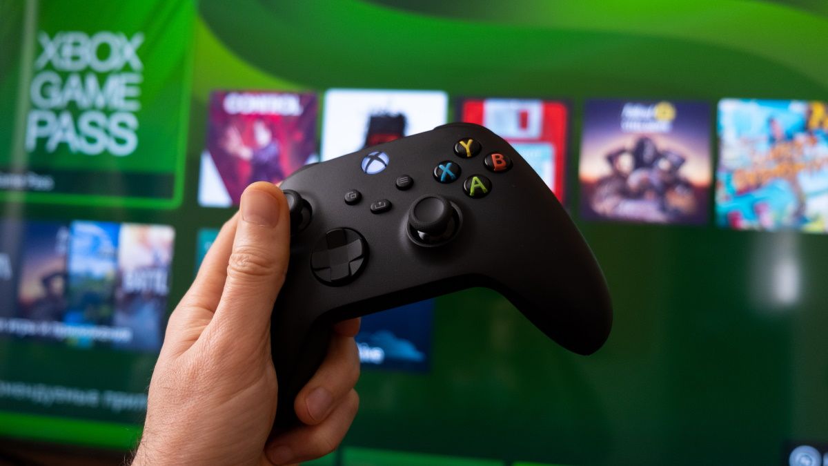 A hand holding an Xbox Series X controller in front of Game Pass on the console.