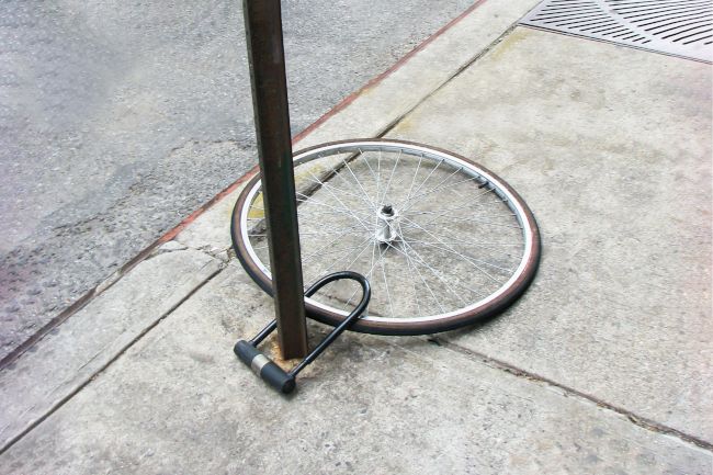 A single bicycle wheel attached to a pole with a bike lock, the rest of the bike presumably stolen.
