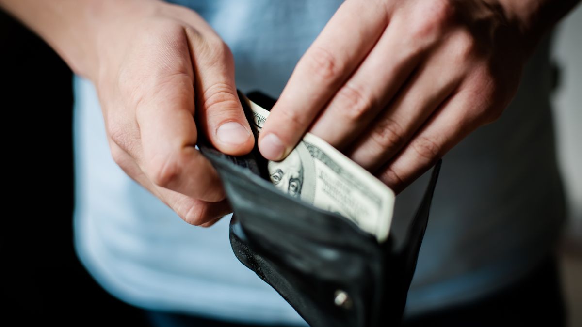 Person&rsquo;s hands pulling a $100 bill out of a wallet.