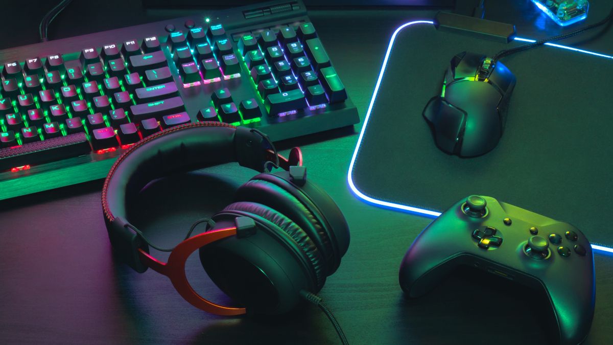 An RGB-lit keyboard, gaming headset, mouse, and controller on a desktop.