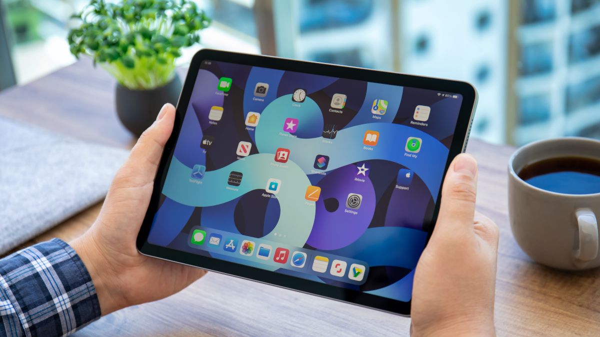 Person's hands holding an iPad with the home screen visible.