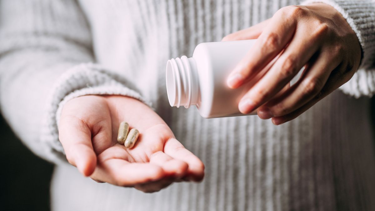 Person's hands holding medicinal herb pills and a white plastic bottle.