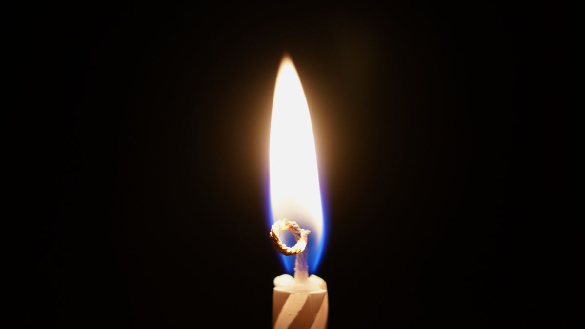 A single flame on a striped birthday candle against a dark background.