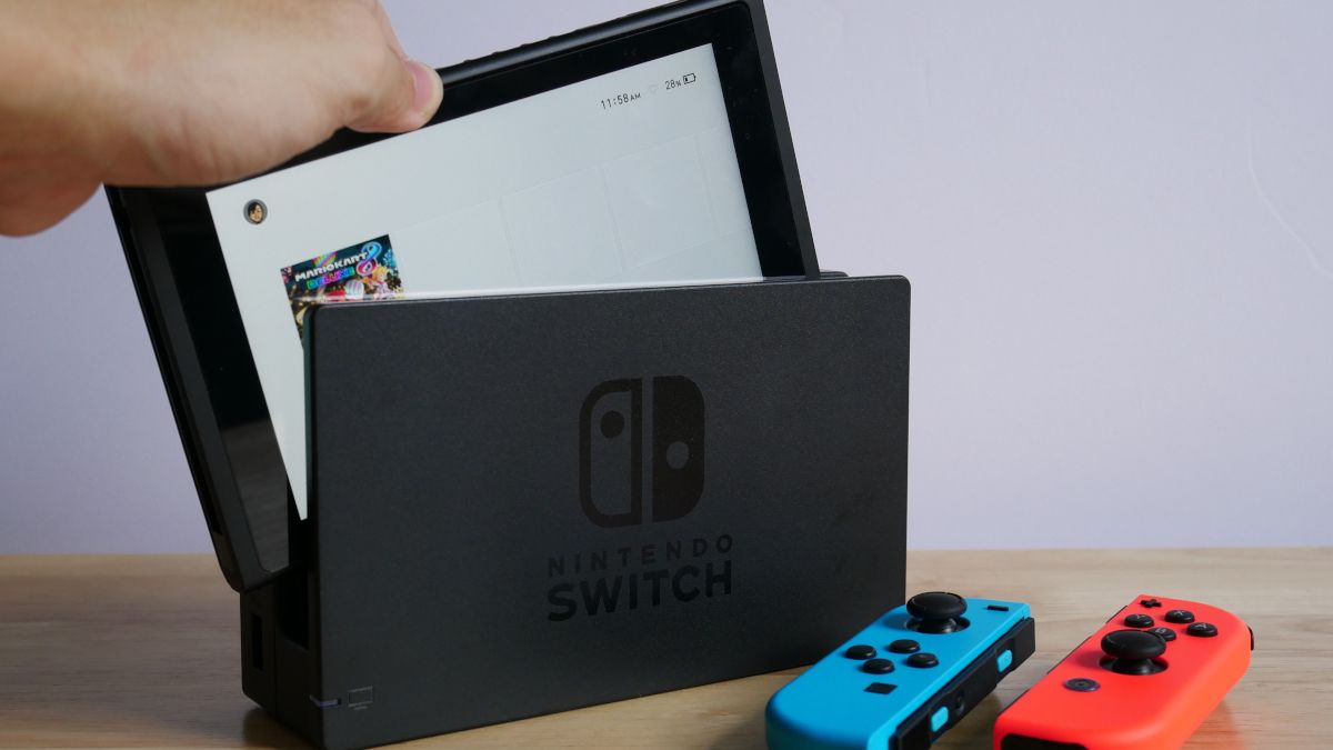 Person's hand putting a Nintendo Switch into its dock, next to blue and red controllers.