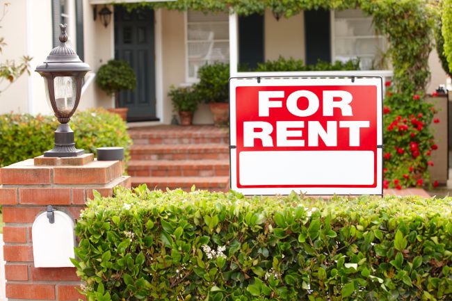 A sign reading "For Rent" in front of a home.