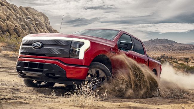 A red 2022 Ford F-150 Lightning electric pickup truck driving through a desert.