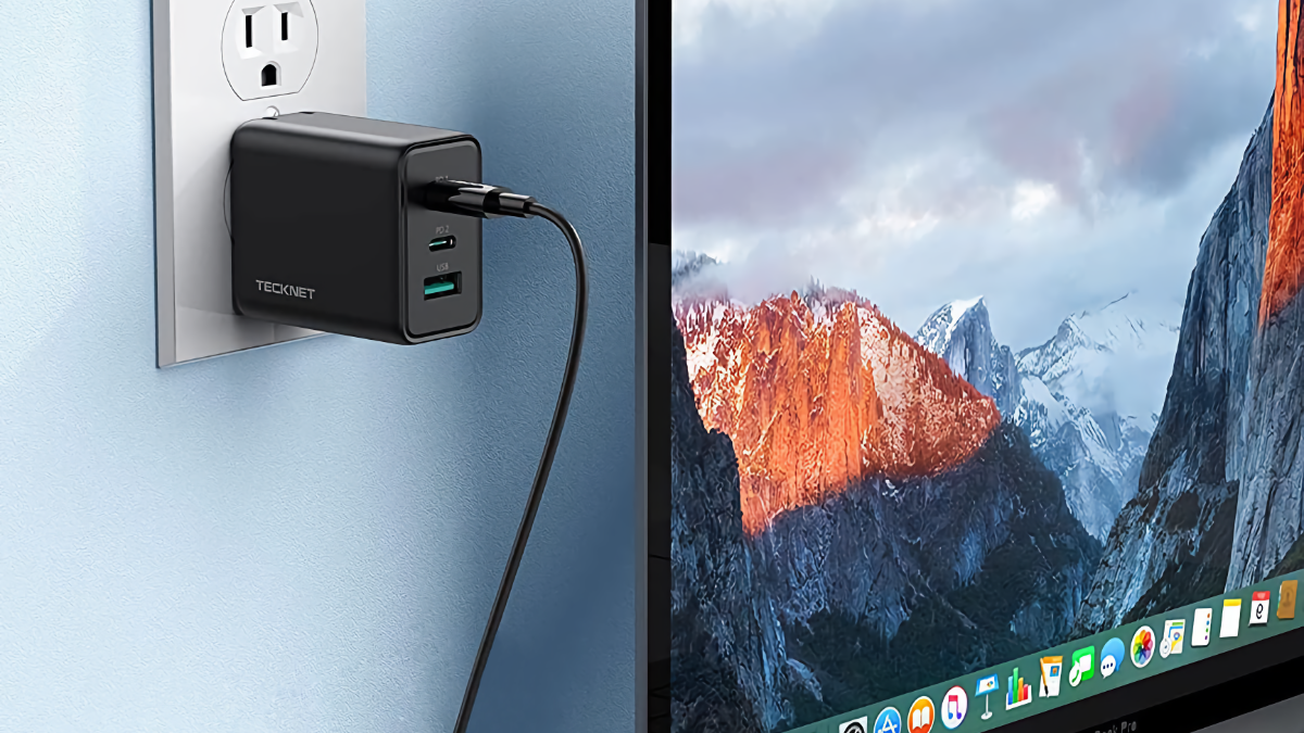 TECKNET 65W USB-C Charger plugged into a wall outlet beside a MacBook