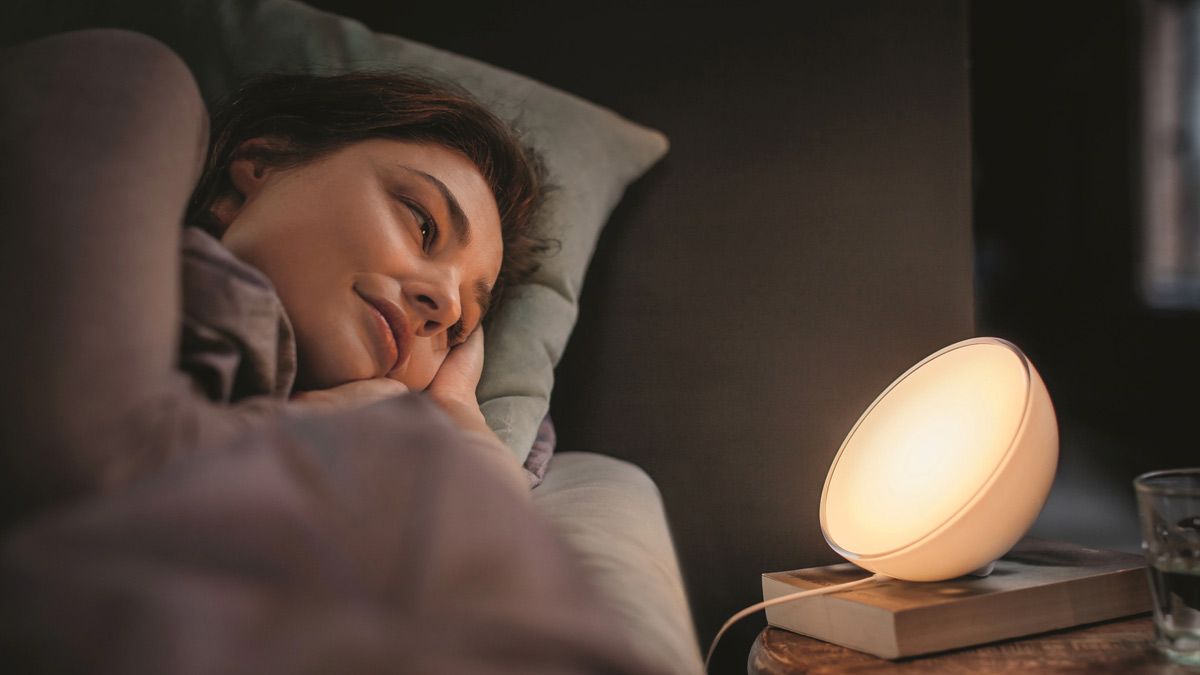 A woman prepares for sleep, looking at a glowing Hue Go smart light on her nightstand.