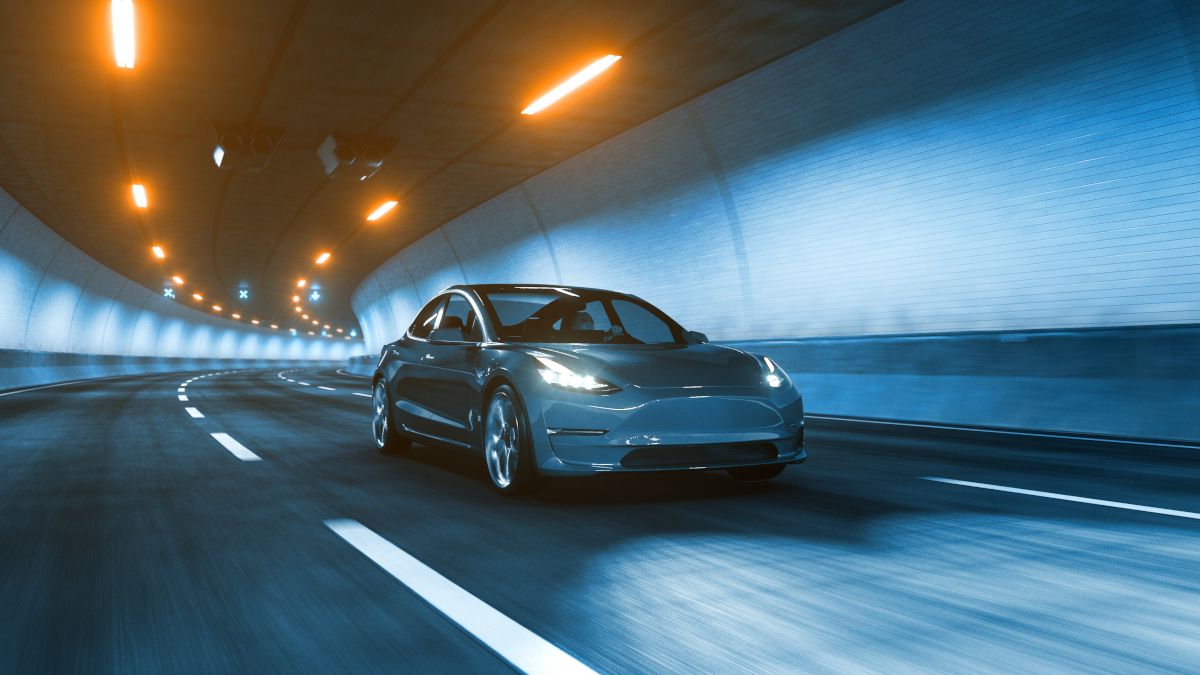 An electric car driving through a tunnel under warm yellow lights.