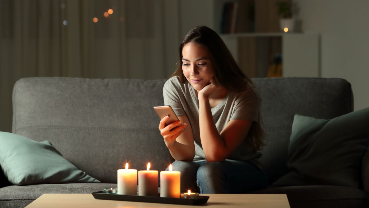 Woman using a smartphone in a living room decorated with lit candles..