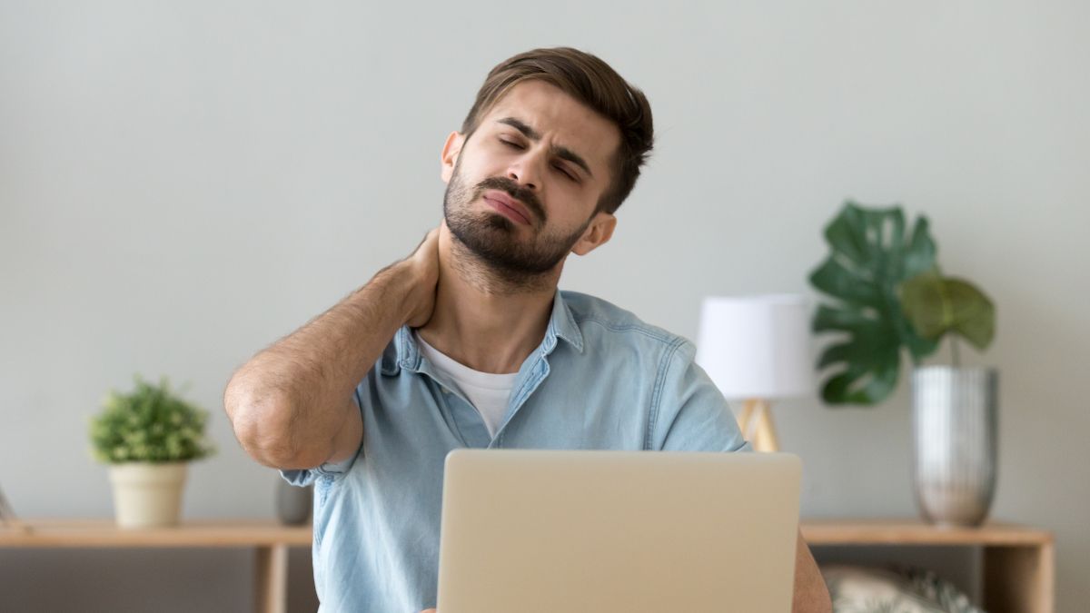 Man sitting in front of a laptop and rubbing his neck in pain.