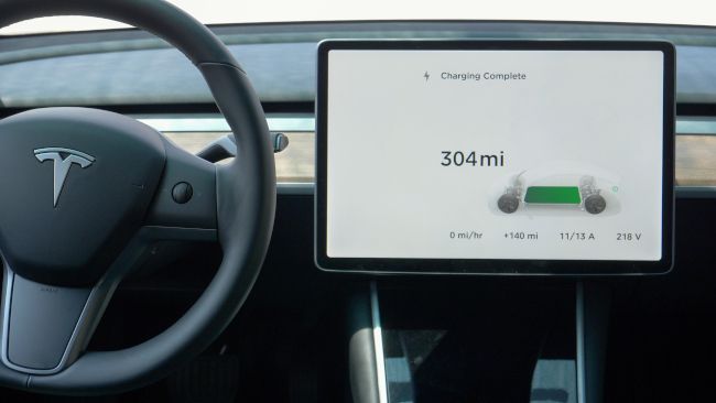 Touchscreen next to the steering wheel inside a Tesla car with a "Charging Complete" message onscreen.