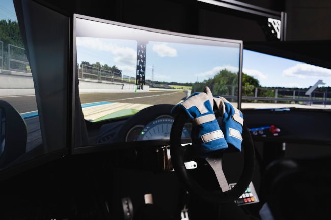 Interior of a racing simulator setup with driving gloves on the steering wheel.