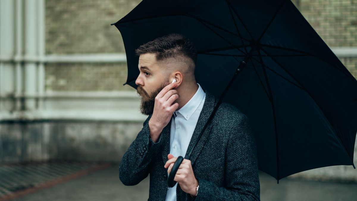 Man putting AirPods in his ear while holding an umbrella in the rain.