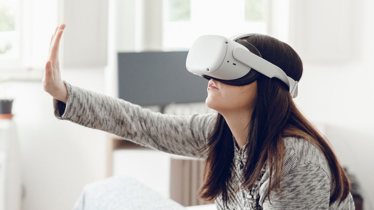 Woman wearing a Meta Quest headset and using her hand to touch the air.