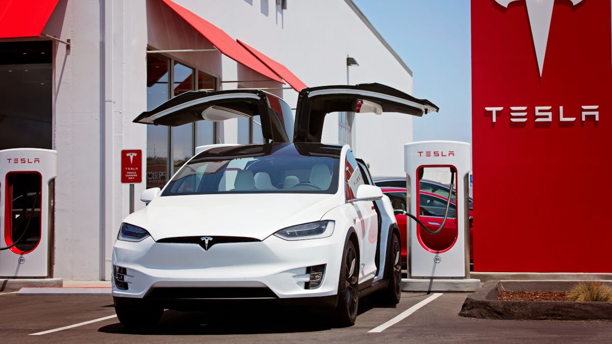 Tesla car plugged into a charging station and with falcon wing doors open.