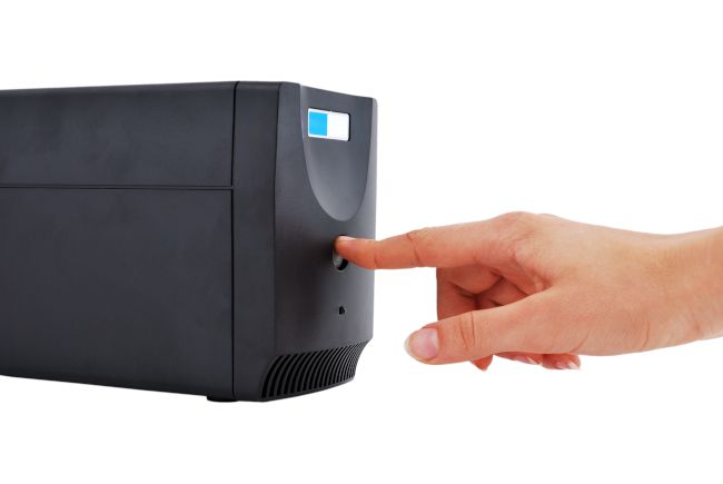 Person's hand pressing a button on an uninterruptible power supply (PSU).